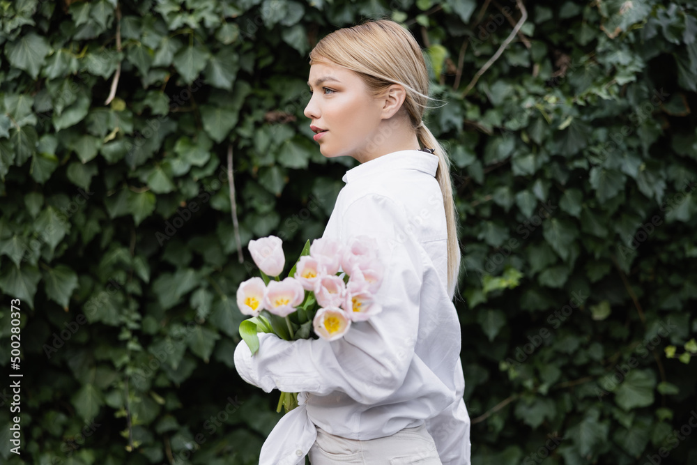 side view of young woman with white tulips near green ivy outdoors. side view of young woman with white tulips near green ivy outdoors.