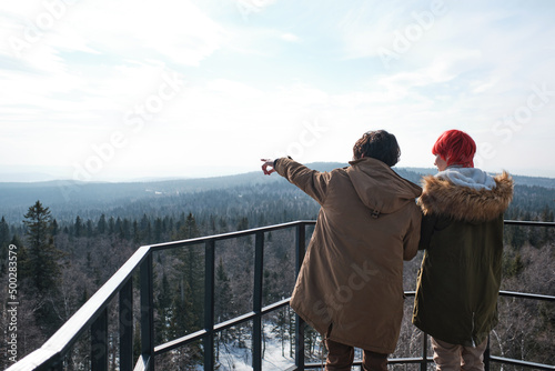 Fototapeta Young man and woman in love standing at observation deck somewhere in mountains