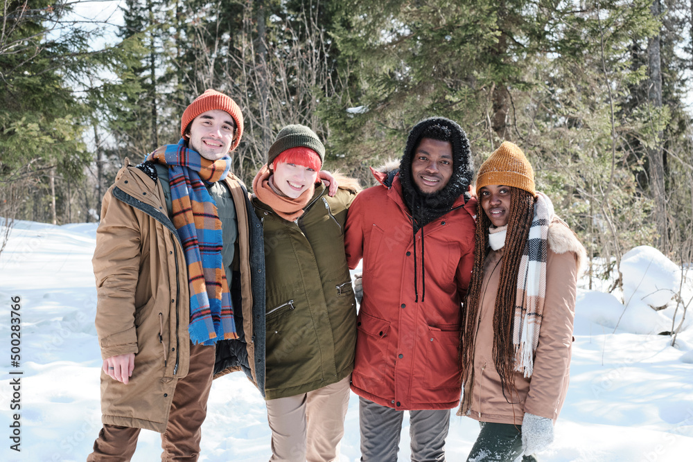 Portrait of joyful young African American and Caucasian men and women spending winter day together somewhere in mountains