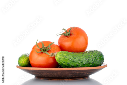 Two ripe tomatoes and two cucumbers on a clay plate  macro  isolated on a white background.