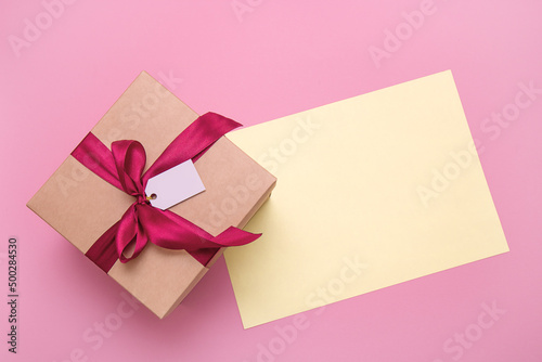 gift box with satin bow and empty tag on pink background with copy space