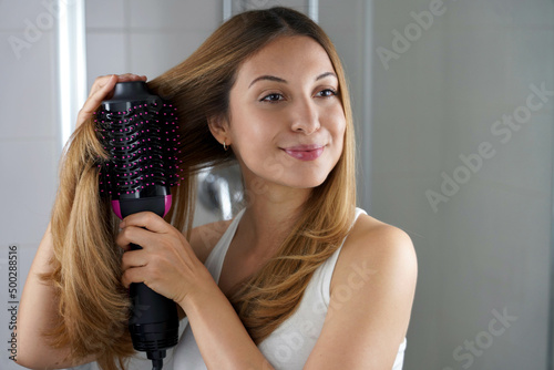 Girl using brush hair dryer to style hair at the mirror on bathroom photo
