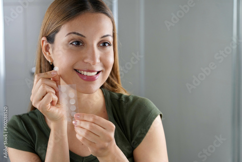 Canvas Print Smiling girl applying acne treatment anti-pickel patch on a pimple in bathroom a