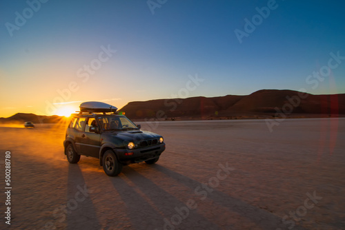 Fototapeta Naklejka Na Ścianę i Meble -  An all-terrain vehicle driving fast through the desert at sunset