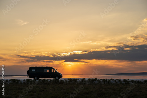 Backlighting silhouette of a 4x4 camper van in a desert landscape at sunset