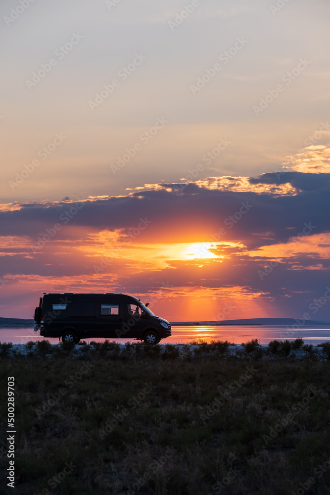 Backlighting silhouette of a camper next to a salt lake at sunset