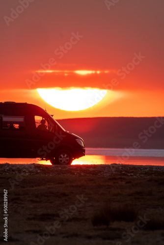 Backlighting silhouette of a camper next to a salt lake at sunset with the sun reflecting in it