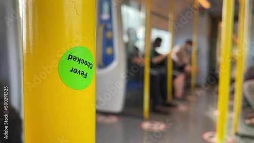 Wallpaper Mural BANGKOK, THAILAND - Circa January, 2022: "Fever Checked" green sticker on yellow pole on public train. Close up shot sticker inside moving Airport rail Link Train on a sunny day. Blurred passengers Torontodigital.ca