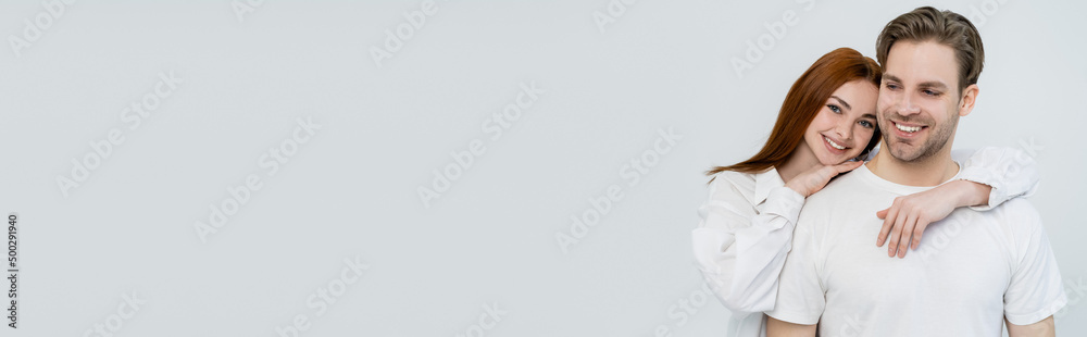 Smiling woman embracing boyfriend and looking at camera isolated on white, banner. Smiling woman embracing boyfriend and looking at camera isolated on white, banner.
