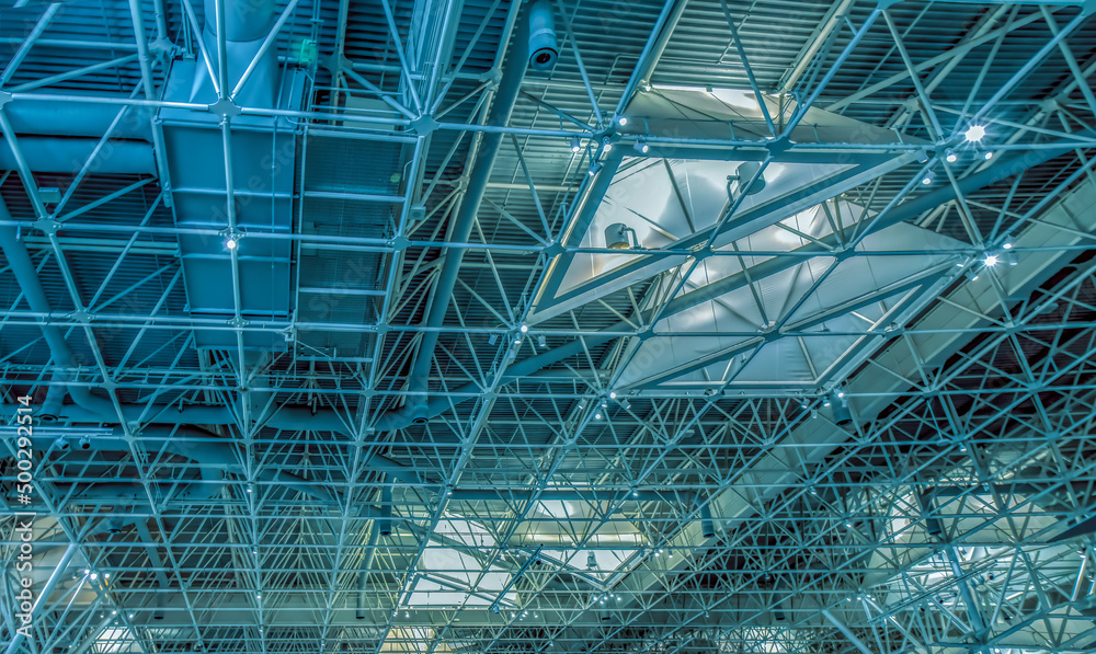 Steel roof structure seen from interior with exposed structural steel tubing, ventilation ducts and industrial light fixtures, nobody Steel roof structure seen from interior with exposed structural steel tubing, ventilation ducts and industrial light fixtures, nobody