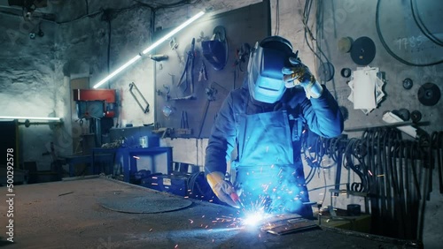 portrait shot of a tired factory worker. steel structure welding, making homemade armor plate by professional worker using welding machine, iron welding, sparks in heavy industry factory indoors