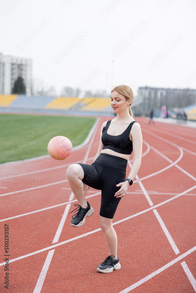full length view of woman in black sportswear playing with ball on athletic field.