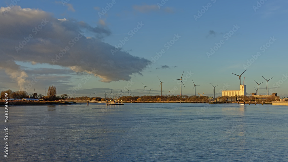Dock in the port of Antwerp, Belgium, with old industrial buildings and wind turbines in warm evening sun light 