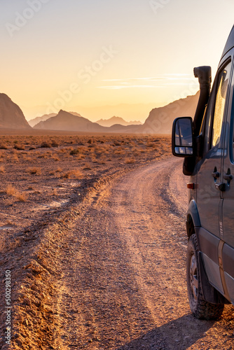 Rugged reliefs of the mountains in the Iranian desert at sunset with a 4x4 camper van on the side photo