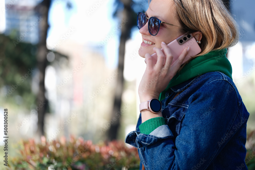 Woman in sunglasses smiling and talking on mobile phone in park