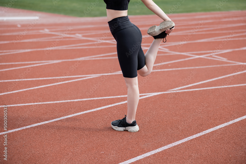 cropped view of sportswoman in black bike shorts stretching leg on stadium.