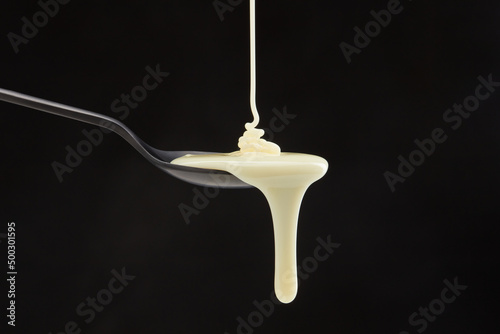 Sweetened condensed milk pouring down from spoon on a black background. Coconut milk with droplet. Shallow depth of field photo