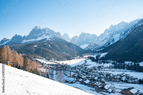 Skier skiing with snow covered house in background. Beautiful white landscape covered in snow. Trees on mountains against sky in alpine region during winter. © Aerial Film Studio