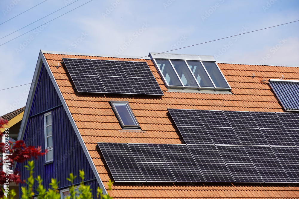 Fototapeta premium Ökologisches Holzhaus mit Photovoltaik Modulen und Solarthermie Panelen auf dem Ziegeldach