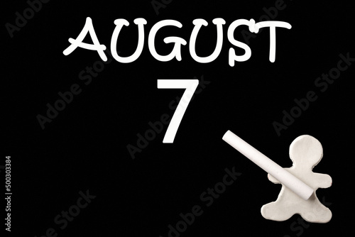 A small white plasticine man writing the date 7 August on a black board. Business concept. Education concept.