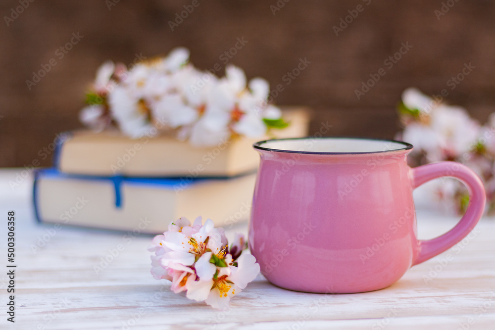 close-up pink cup and a blossoming spring twig of an almond tree on a table next to books. spring still life close-up pink cup and a blossoming spring twig of an almond tree on a table next to books. spring still life