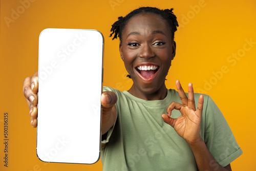 Young smiling african american woman showing smartphone with blank screen against yellow background