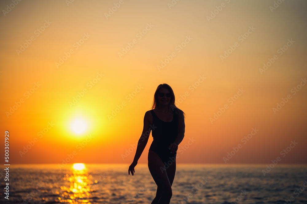 Silhouettes of a girl against the background of the sea and the setting sun. Selective focus