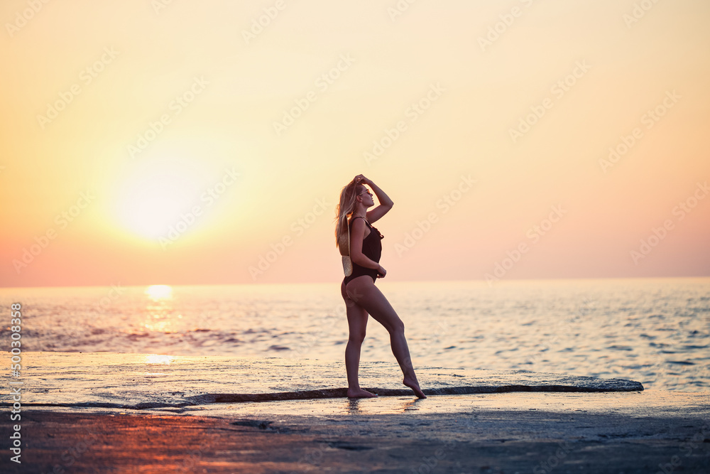 Beautiful lady in a black swimsuit on the seashore, Smiling face, with a straw hat on her shoulders. Golden sunset light
