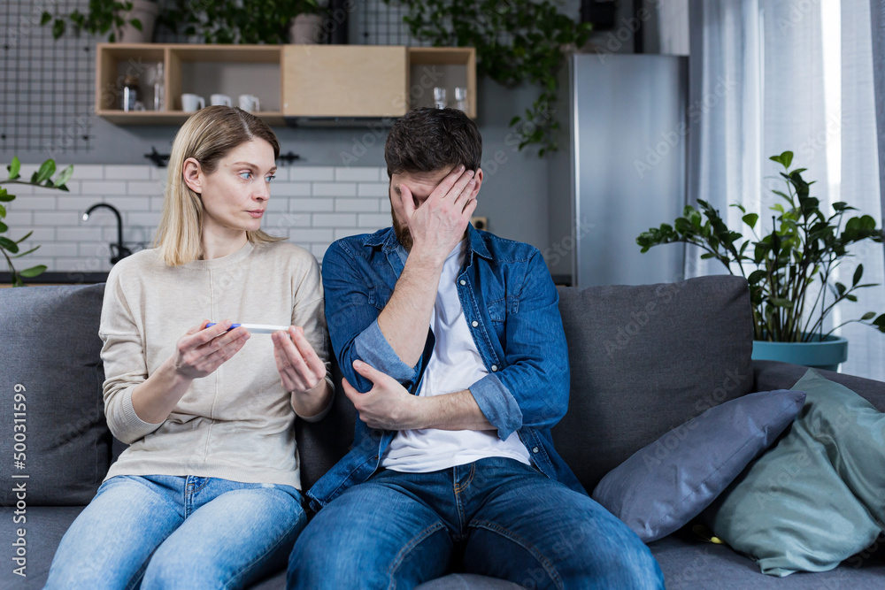 Frustrated man and woman sitting on the couch at home, received a negative pregnancy test Frustrated man and woman sitting on the couch at home, received a negative pregnancy test