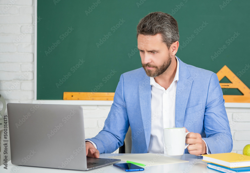 school tutor in classroom with laptop having coffee break