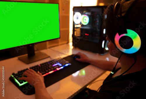 Playing on computer, teenage gamer boy playing on computer in his room at night. Room and computer has warm neon lights. 