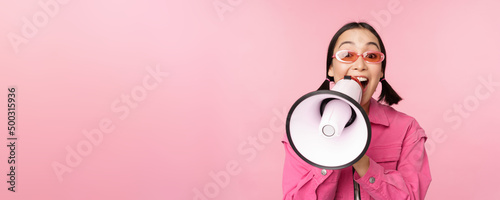Attention, announcement concept. Enthusiastic asian girl shouting in megaphone, advertising with speaker, recruiting, standing over pink background