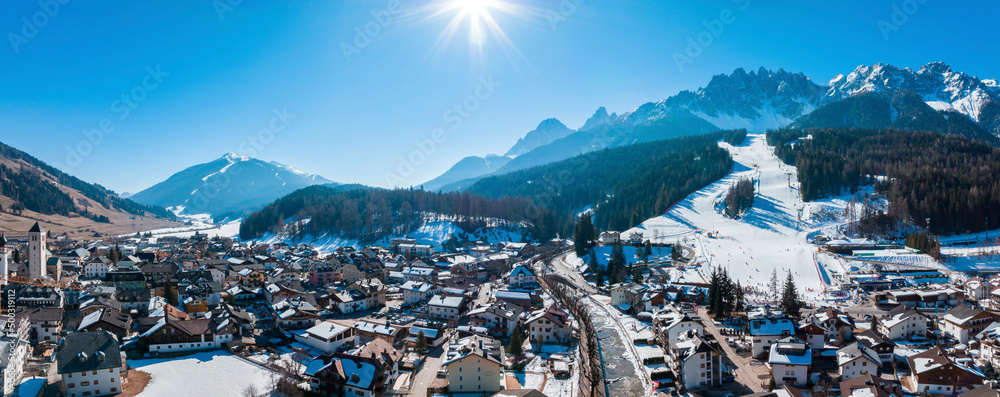Scenic view of sun shining on village in south tyrol against clear blue sky. Crowded houses against snow covered mountains on sunny day. Beautiful townscape in alps during winter.