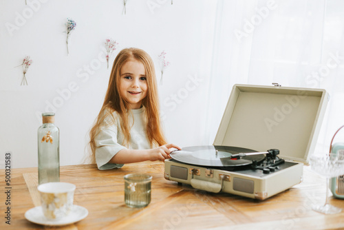 little red haired girl near record player in kitchen of rustic country house with beautiful vintage decor, a happy todler girl in spring, earth tone colors © klavdiyav