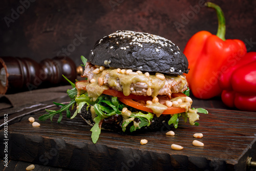 Black Burger with meat patty, tomatoes, aragula and sauce on dark board photo