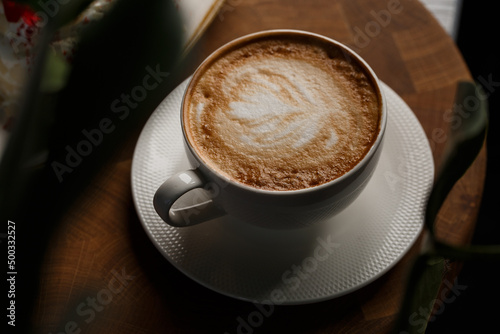 White cup of hot latte coffee with beautiful milk foam latte art texture isolated on dark background. Overhead view, copy space. Coffee shop menu.