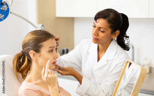 Latin woman beauty doctor looking at caucasian woman's face during examination.