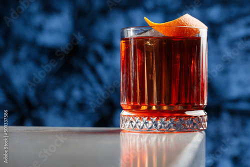 Crystal glass with bright cold alcoholic cocktail decorated with orange zest. Blurred background. Negroni cocktail