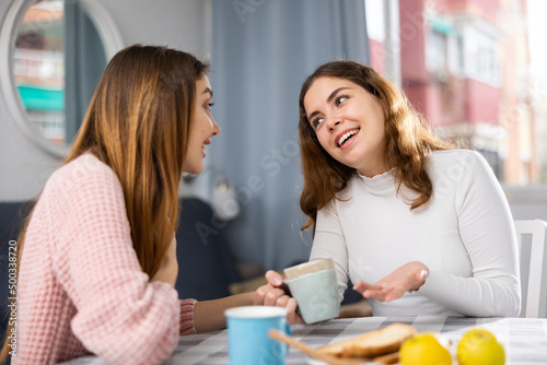 Two girlfriends talking and drinking tea together, spending day together at home