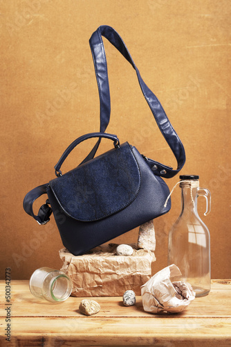 Still life with blue women's handbag and objects made of natural materials and glass. Eco leather handbag and objects on wooden table.