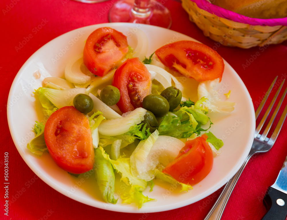 Traditional Valencian salad with lettuce leaves, sliced ​​tomatoes, onion and olives with olive oil