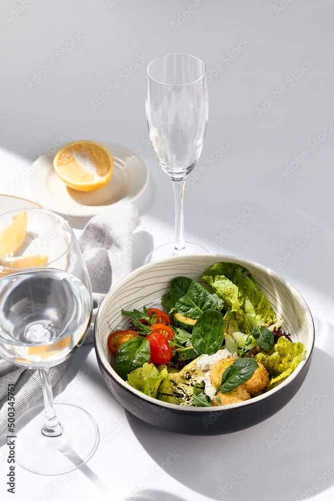 Salad bowl with avocado, tomato and cheese balls. Healthy vegetarian lunch with water glass on white table. Summer day dinner, sunlight and harsh shadow. Healthy salad bowl food. Organic salad bowl. Salad bowl with avocado, tomato and cheese balls. Healthy vegetarian lunch with water glass on white table. Summer day dinner, sunlight and harsh shadow. Healthy salad bowl food. Organic salad bowl.