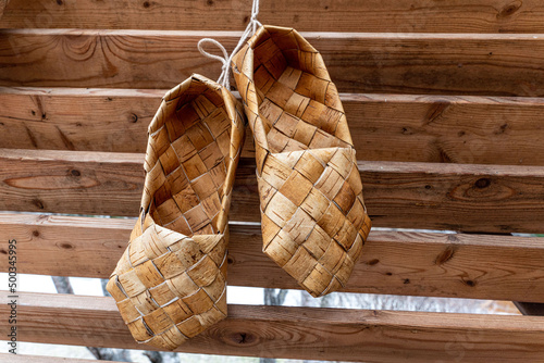 Birchen woven bast shoes hang on a log wall. photo
