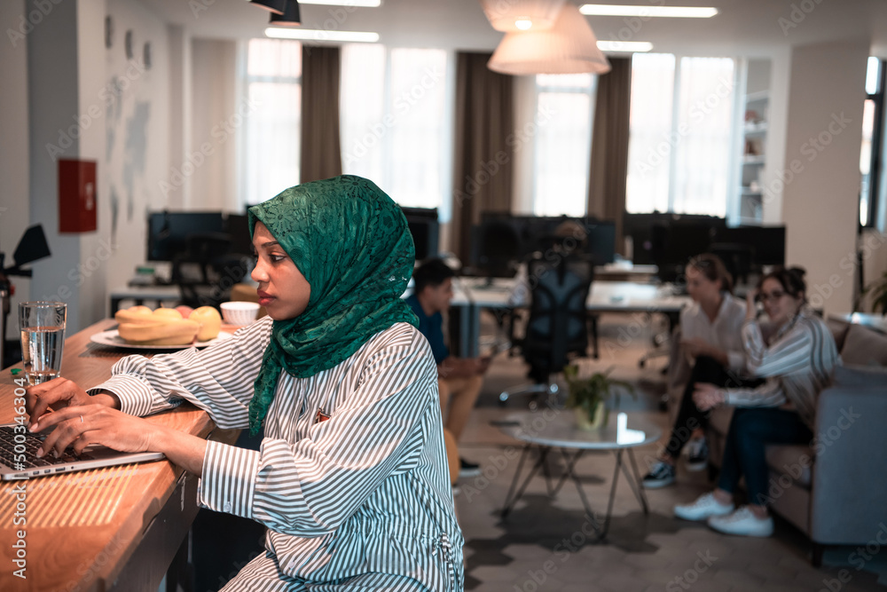 African Muslim business woman wearing a green hijab and working on laptop computer in relaxation area at modern open plan startup office. African Muslim business woman wearing a green hijab and working on laptop computer in relaxation area at modern open plan startup office.