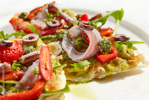 Tapas with avocado cream, anchovy, paprika and kalamata olives on focaccia. Bruschetta with guacamole and anchovy isolated on white background. Appetizer contemporary concept. Fish antipasti.