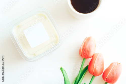 White chocolate in plastic container next to coffee and tulips.