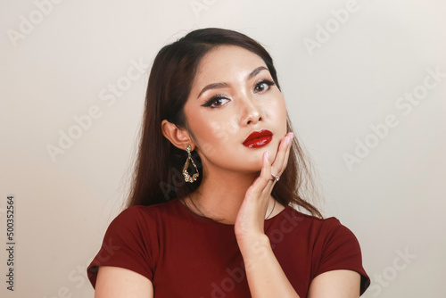 A fierce-looking Asian woman in a red shirt posing in front of white background