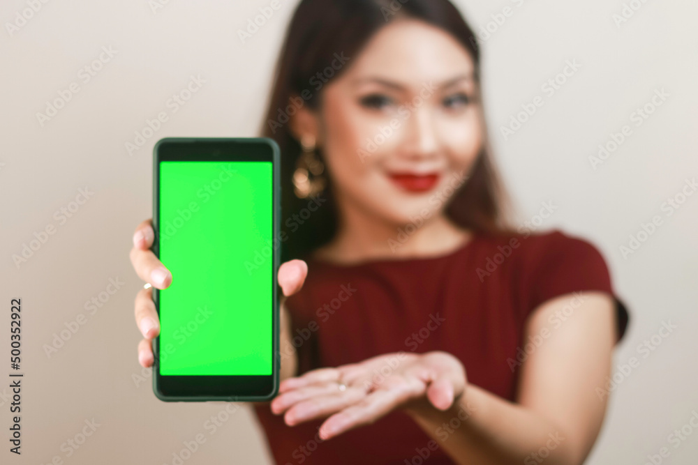 Happy and smiling young Asian woman showing and pointing to a green blank screen.