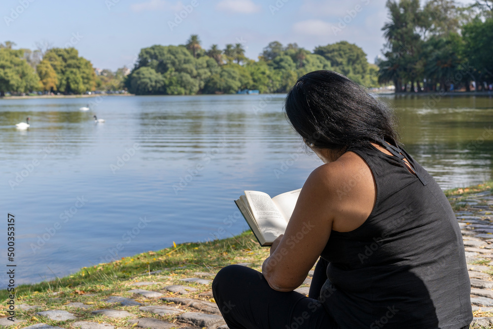Mature latin woman reading a book sitting in a lake