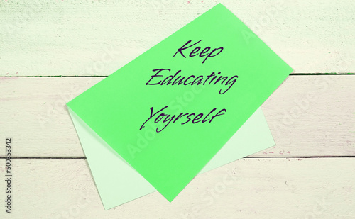 Keep Educating Yourself text. Asymmetrically folded sheet on wooden  board surface, personal development concept